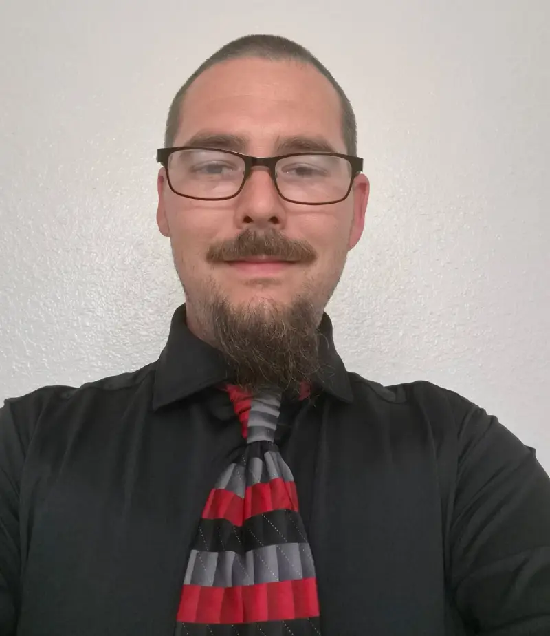 A smiling man with a gray beard in a white shirt.